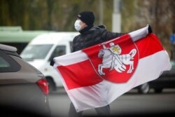 FILE - A man wearing a face mask to help curb the spread of the coronavirus holds an old Belarusian national flag during an opposition rally to protest the official presidential election results in Minsk, Nov. 22, 2020.
