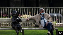 A man relaxes on a bench in London, next to a sculpture of Paddington Bear, as the country is in lockdown to help curb the spread of the coronavirus, April 15, 2020. 