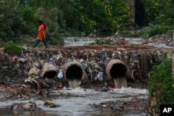 A woman walks over drainage pipes that flow into the Bagmati River in Kathmandu, Nepal, Wednesday, June 1, 2022. (AP Photo/Niranjan Shrestha)
