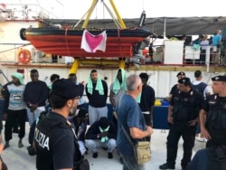 Migrants stand on the quay after disembarking from the Dutch-flagged Sea-Watch 3 ship, at the Lampedusa harbor, Italy, Saturday, June 29, 2019.