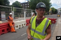 FILE - In this photo taken June 24, 2016, Iosif Achim, a 32-year-old Romanian logistics manager, right, stands at a construction site while being interviewed in London.