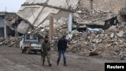Rebel fighters walk near damaged buildings in al-Rai town, northern Aleppo countryside, Syria, Dec. 30, 2016. 