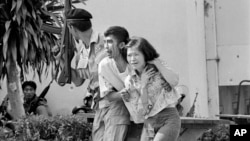 FILE - In this Oct. 6, 1976 file photo blood streaming down his face, a leftist student, center, wounded and captured by police is helped to an ambulance at the Thammasat University campus in Bangkok, Thailand.