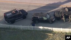 Armored vehicles surround an SUV following a second shootout in which two suspects were killed and a police officer was wounded.