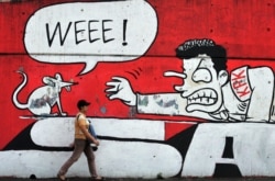 Seorang perempuan berjalan melewati tembok yang dihiasi grafiti yang menunjukkan dukungan terhadap gerakan antikorupsi pemerintah di Jakarta, 20 Juli 2010. (Foto: AFP/Bay Ismoyo)