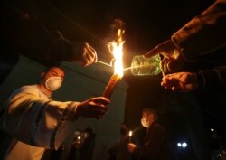 A clergyman and believers wearing protective masks hold candles outside a church during an Orthodox Easter service, amid the coronavirus disease outbreak in Marneuli, Georgia, April 19, 2020.