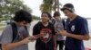 FILE -- Brian Vega, left, Peyton Ruiz, second from left, and Max Marrero, right, check their smartphones at Bayfront Park in downtown Miami, Florida.