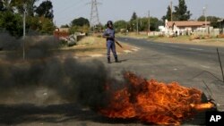 A police officer stands on a barricaded street as tires burn during a protest in Ennerdale town township, Johannesburg, South Africa, May 11, 2017.