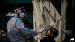 Petugas kesehatan mengambil sampel swab penumpang untuk tes COVID-19 di stasiun kereta api di New Delhi, India, Kamis, 30 Desember 2021. (Foto: AP/Altaf Qadri)