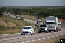 A Russian aid convoy of trucks is escorted by a police vehicle as they travel on a road to the border control point in the Russian town of Donetsk, in the Rostov-on-Don region, Russia, Aug. 17, 2014.