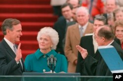 FILE - President George H.W. Bush raises his right hand as he is sworn into office as the 41st president of the United States by Chief Justice William Rehnquist outside the west front of the Capitol as first lady Barbara Bush holds the bible for her husband, Jan. 20, 1989.