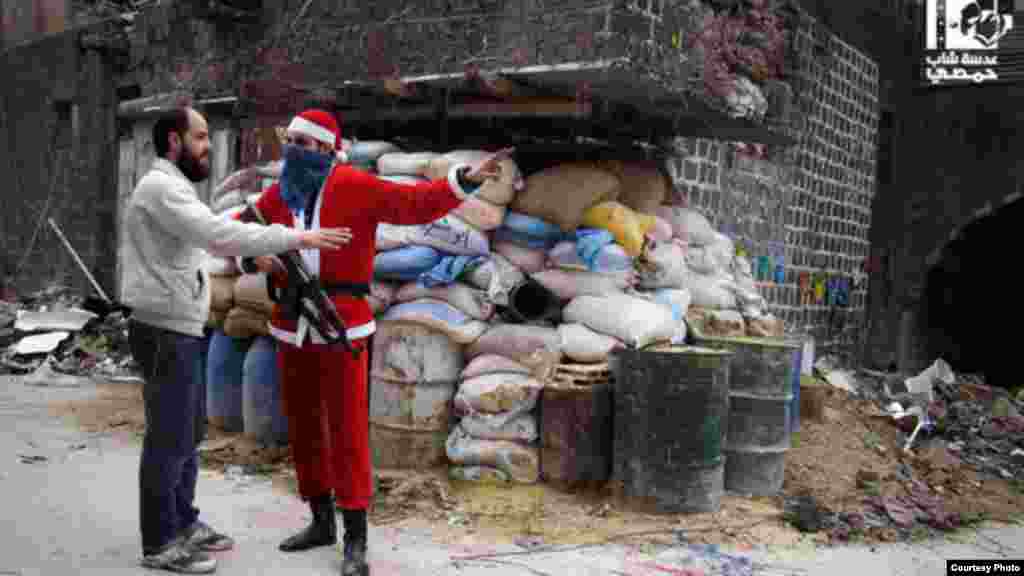 Seorang anggota Tentara Pembebasan Suriah dalam kostum sinterklas menunjukkan arah pada warga Homs di daerah kota tua (1/1). (Lens Young Homsi)
