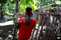 Janila Jean, 18, carries her daughter as she walks to her friend's house before an interview in Jacmel, Haiti, Aug. 15, 2016.