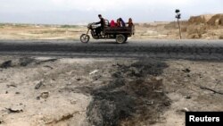 An Afghan family ride on a bike past the site of a car bomb attack where U.S. soldiers were killed near Bagram air base, Afghanistan, April 9, 2019.