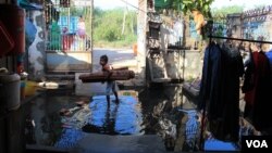A girl stands in a flood of water, holding a sleeping mat, in front of Khoeun Sovat’s house in Boeung Kak community in Phnom Penh, Cambodia, Nov. 13, 2014. (Nov Povleakhena/VOA Khmer)