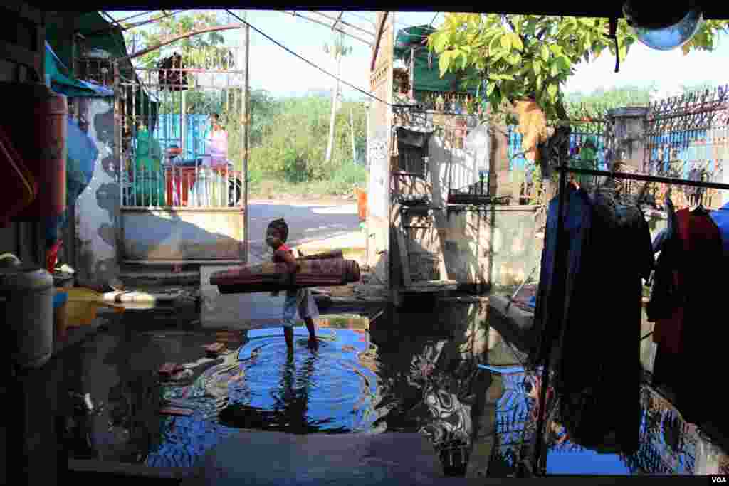 A girl stands in flood water, holding a sleeping mat in front of Khoeun Sovat&rsquo;s house in Boeung Kak community in Phnom Penh, Cambodia, Nov. 13, 2014. (Nov Povleakhena/VOA Khmer)