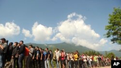 In this file photo dated June 19, 2019, migrants and refugees wait in line to receive supplies from the Red Cross at the Vucijak refugee camp outside Bihac, western Bosnia.