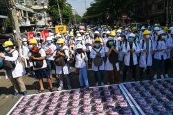 Nakes dan mahasiswa berdiri di depan potret Pimpinan Angkatan Bersenjata Myanmar Jenderal Senior Min Aung Hlaing yang ditempatkan di jalan selama aksi protes menentang kudeta militer di Yangon, 5 Maret 2021. (Foto: STR / AFP)