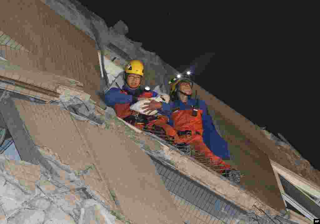 Rescue workers carry a baby swaddled in a cloth from the rubble of a toppled building.