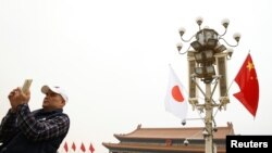 A man uses his mobile phone under Chinese and Japanese flags in front of the Tiananmen Gate ahead of Japan's Prime Minister Shinzo Abe's visit, in Beijing, Oct. 25, 2018.