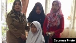 Bulan mencoba kursi roda baru yang dikirim Presiden Joko Widodo untuknya hari Selasa (20/3) didampingi kepala sekolah (kanan) dan ibundanya (berkerudung merah). (Courtesy: Bulan Karunia)