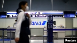 Seorang karyawan, mengenakan masker pelindung setelah wabah Covid-19), lewat di depan loket All Nippon Airways (ANA) di Bandara Internasional Kansai yang hampir kosong di Osaka, Jepang, 14 Maret 2020. (Foto: Reuters)