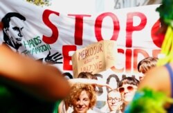 FILE - Climate activists of the Extinction Rebellion group hold signs, including "Mercosur sells Amazon," outside the embassy of Brazil in Brussels, Belgium, Aug. 26, 2019.