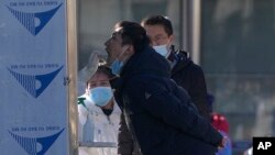 Residents wearing face masks watch a man getting a throat swab at a coronavirus testing site in Xicheng district in Beijing, China, Jan. 27, 2022.