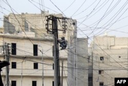FILE - A man tries to fix electrical wires in the Salaheddin neighborhood of the northern Syrian city of Aleppo, Jan. 27, 2014.