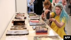 Visitors take pictures of damaged books of the Kharkiv publishing house, which were destroyed by Russian shelling on May 23, during the opening of the annual publisher's forum "Book Arsenal" in Kyiv, on May 30, 2024, amid the Russian invasion in Ukraine. 
