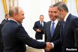 ولادیمیر پوتین، رئیس جمهوری روسیه، در حال دست دادن با هاکان فیدان، رئیس دستگاه اطلاعاتی ترکیه و خلوصی آکار وزیر دفاع ترکیه (در سمت راست هاکان فیدان). کاخ کرملین، ۲۴ اوت ٢٠١٨