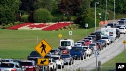 A line of vehicles wait to enter Canada at the Peace Arch border crossing in view of a Canadian flag made of flowers Monday, Aug. 9, 2021, in Blaine, Wash. 