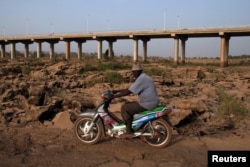 FILE - A man rides a motorcycle on a dry riverbed under a bridge in Bamako, Feb. 26, 2014.