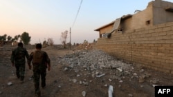 FILE - Peshmerga fighters walk past a damaged house in an Iraqi Kurdish Kakai minority village located near the town of Kalak, east of Mosul, Oct. 26, 2016.