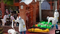 Family members watch as Nepalese army personnel in protective suits prepare the bodies of COVID-19 victims for cremation, near Pashupatinath temple, in Kathmandu, Nepal, May 7, 2021.