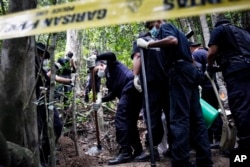 A Malaysian police forensic team excavates an unmarked grave in Wang Burma at the Malaysia-Thailand border outside Wang Kelian, Malaysia on Tuesday, May 26, 2015. (AP Photo)