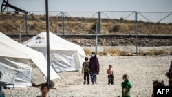 FILE - A woman clad in a mask due to the COVID-19 pandemic walks next to a child by tents at Camp Roj, housing people who were relocated from al-Hol camp, in Syria's northeastern Hasakah province, Sept. 30, 2020.