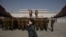 FILE - A woman talks on a mobile phone as Korean People's Army soldiers gather for a memorial tribute before the statues of late North Korean leaders Kim Il Sung and Kim Jong Il, on Mansu hill in Pyongyang, North Korea, April 15, 2019. 