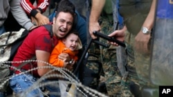 ជន​ទេសន្តរប្រវេសន៍​ម្នាក់​ដែល​អោប​ក្មេង​ប្រុស​ម្នាក់​ប្រតិកម្ម​ទៅ​ប៉ូលិស​ កំឡុង​ការ​ប៉ះ​ទង្គិច​គ្នា​នៅ​ក្បែរ​ស្ថានីយ៍​រថភ្លើង​នៅ​ព្រំដែន​ ភាគ​ខាង​ជើង​នៃ​ប្រទេស​ក្រិក​ កាលពី​ថ្ងៃទី២១ ខែសីហា ឆ្នាំ២០១៥។