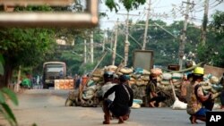Anti-coup protesters squat behind a barricade that separates them from security forces on the opposite side of the road, in the Dala township of Yangon, Myanmar, Mar. 26, 2021.