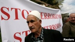 FILE - A Kosovo-Albanian man stands in front of a banner during a protest with the slogan "Stop Terrorism" in Pristina, Kosovo, April 24, 2012. A court in Pristina on Thursday sentenced seven men convicted of terror charges.
