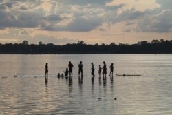 ប្រជាជនដើរលេងក្នុងទឹកទន្លេមេគង្គ ក្នុងខេត្តស្ទឹងត្រែង នាពេលថ្ងៃលិច កាលពីថ្ងៃទី២០ ខែកក្កដា ឆ្នាំ២០២០។ (ស៊ុន ណារិន/វីអូអេ)