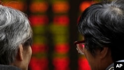 Dua pialang saham perempuan berbicara sambil mengamati pergerakan saham di Bursa Saham Beijing, China, Senin (26/3).