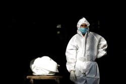 Seorang nakes di India, mengenakan alat pelindung diri (APD), berdiri di samping jenazah seorang pria yang meninggal akibat penyakit COVID-19, sebelum dikremasi di sebuah krematorium di New Delhi, India, 28 September 2020.