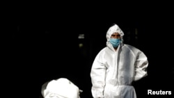 Seorang petugas kesehatan yang mengenakan alat pelindung diri (APD) berdiri di samping tubuh seorang pria yang meninggal akibat Covid-19 sebelum dikremasi di krematorium di New Delhi, India, 28 September 2020. (Foto: Reuters)