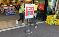 In this May 19, 2021, photo, a shopper pushes her basket filled with purchases past a sign warning of the need to wear face masks while in a food store in Aurora, Colorado. (AP Photo/David Zalubowski)