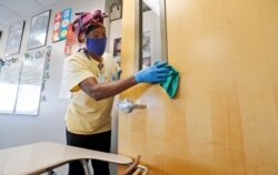 FILE - Amid concerns of the spread of COVID-19, Alma Odong wears a mask as she cleans a classroom at Wylie High School in Wylie, Texas, July 14, 2020.