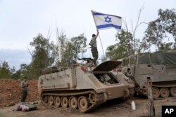 Seorang tentara Israel merapikan bendera nasional sementara tentara lainnya berdoa di dekat perbatasan Israel-Gaza di Israel selatan pada Sabtu, 25 November 2023. (Foto: AP)