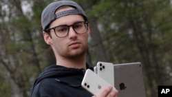 In this Monday, May 4, 2020, photo, Kaya Suner holds up an iPhone and an iPad as he stands for a picture in Northfield, New Hampshire, USA. (AP Photo/Charles Krupa)