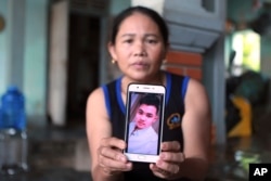 Hoang Thi Ai holds up her phone showing a photo of her son Hoang Van Tiep, who she fears is one of the possible victims in the truck deaths in England, at her home in Nghe An province, Vietnam on Monday, Oct. 28, 2019. (AP Photo/Hau Dinh)